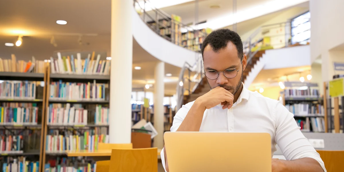 Profissional analisando informa&ccedil;&otilde;es em um laptop em uma biblioteca